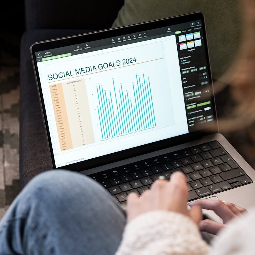 Woman reviewing 2024 social media goals chart on laptop indoors.